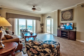 A spacious living room with a large window offering a view of the landscape, a television, and a dining area with a table and chairs.