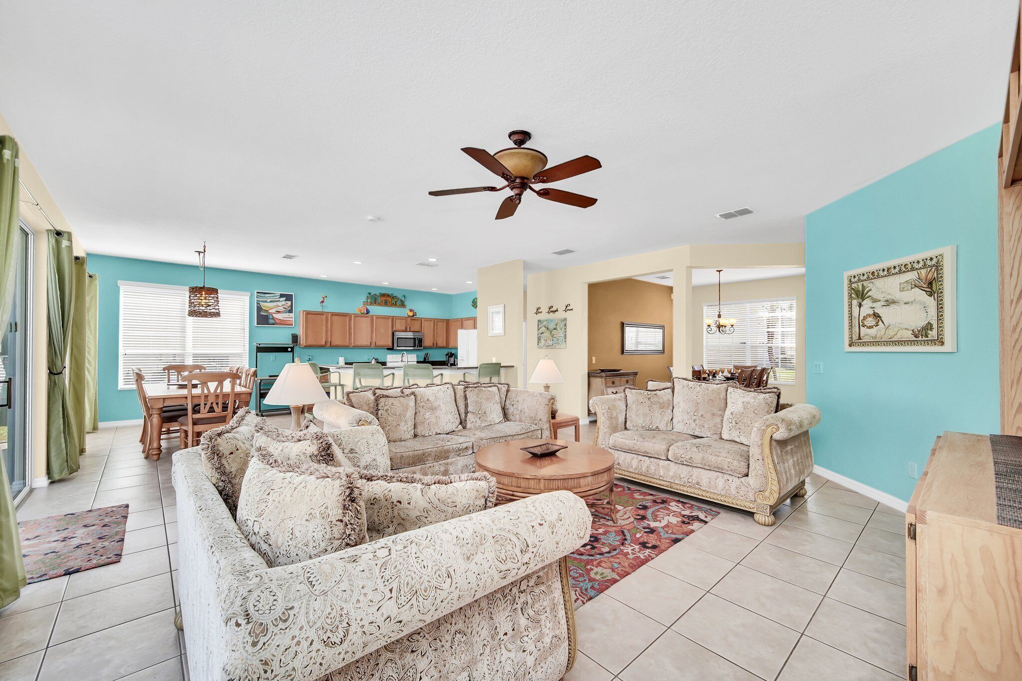 A spacious living area with a ceiling fan, a dining table with chairs, and a kitchen in the background.