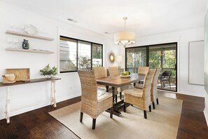 A dining area with a wooden table and wicker chairs, a hanging light fixture, and a view through large windows. - 22 Hollyberry:  A BESTNEST by Beverly Serral (Hilton Head Island)