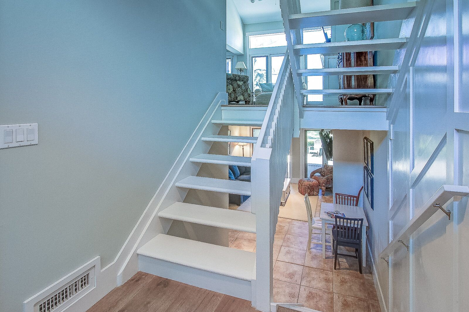 Un escalier avec des rampes blanches menant à un espace situé au deuxième étage, où se trouvent une table à manger et des chaises.