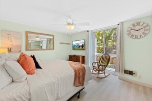 A bedroom with a bed, a rocking chair, a television, and a large window.