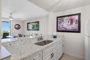 A kitchen with a marble countertop, a sink, and a refrigerator. There is a window with a view of greenery outside. - Ground floor condo with grassy area, quick Beach Access, G33 North Coast Village (Oceanside)