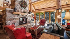 Un salón amplio con chimenea de piedra, mobiliario de cuero y grandes ventanas que ofrecen vistas al exterior.