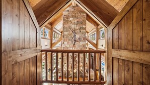 Un interior de madera con chimenea de piedra, vigas de madera y barandilla de balcón.