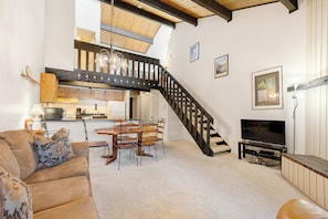 A spacious living area with a dining table, chairs, a sofa, a TV, and a staircase.