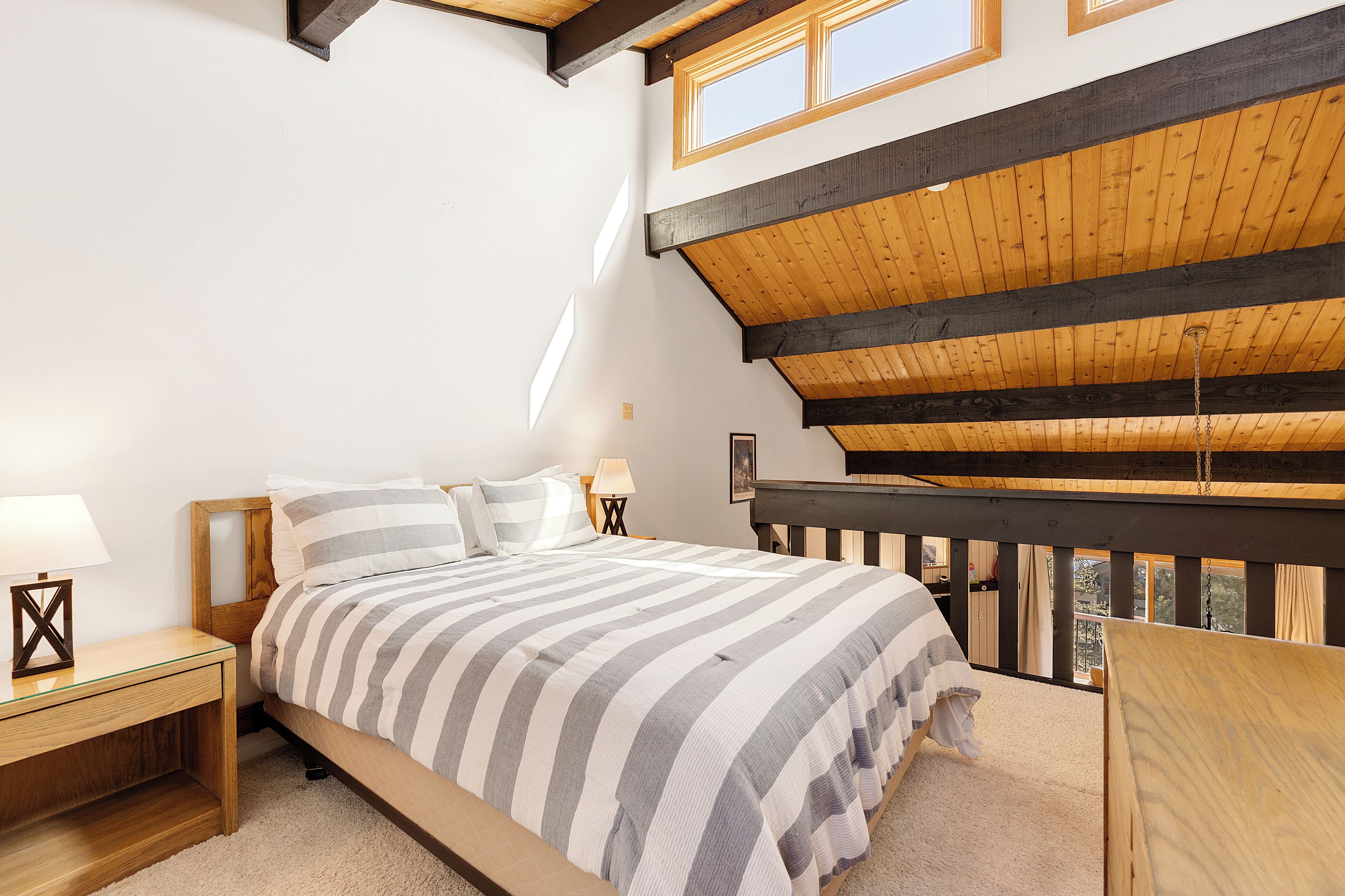 Una camera da letto con soffitto in legno, un letto con lenzuola a righe, un comodino e vista sull'esterno.