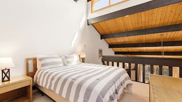 Una camera da letto con soffitto in legno, un letto con lenzuola a righe, un comodino e vista sull'esterno.