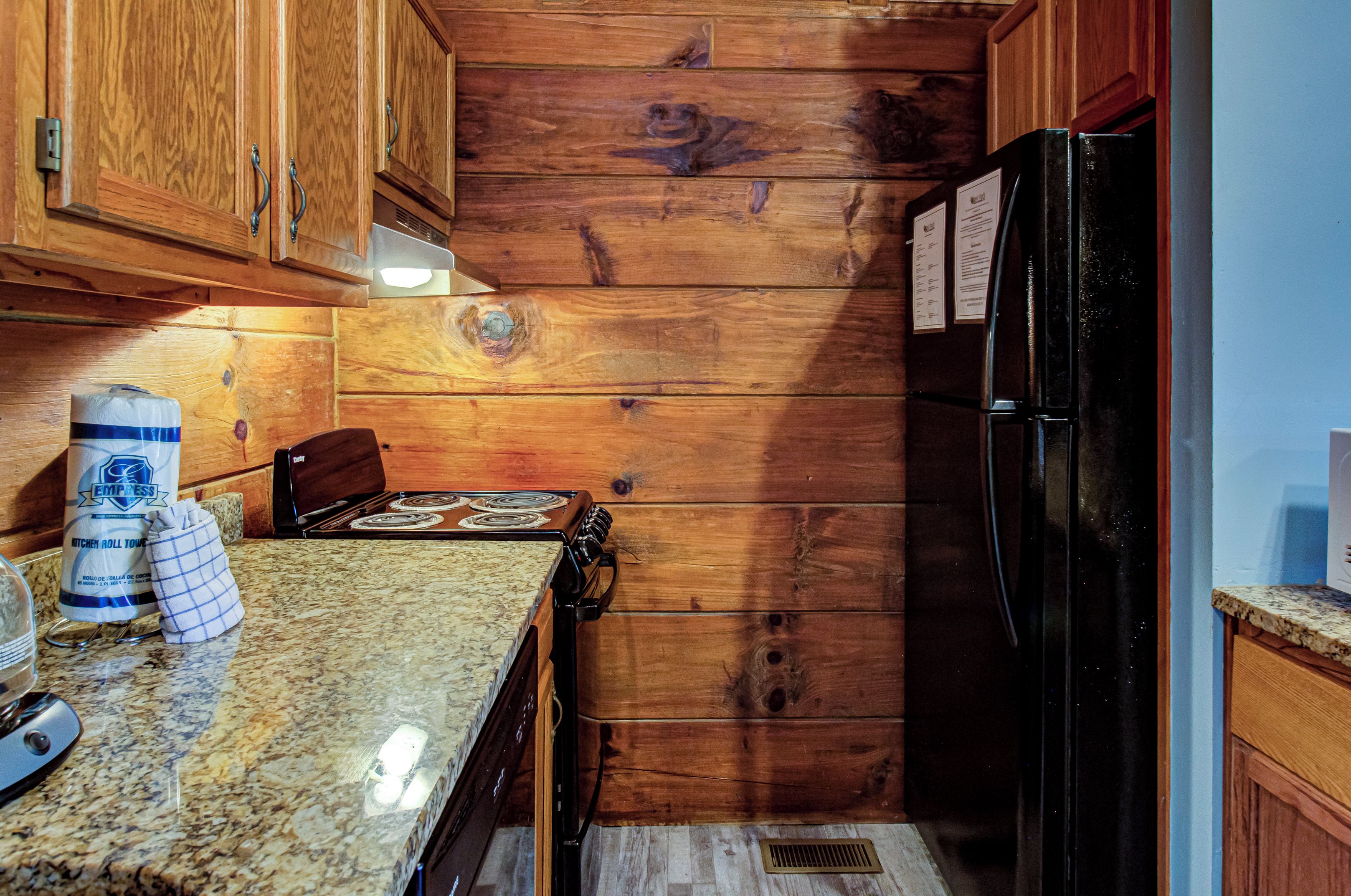 Une cuisine avec des meubles en bois, un réfrigérateur noir, une cuisinière et des plans de travail en granit.
