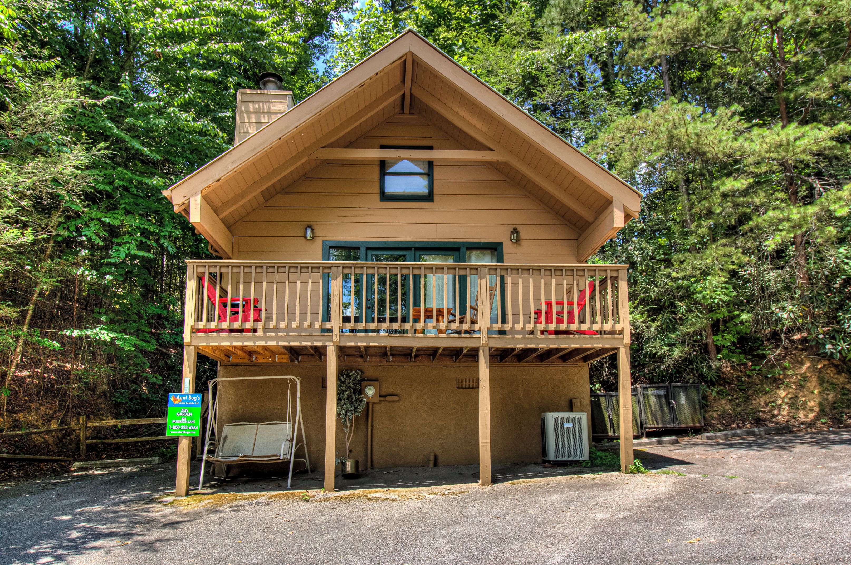 A two-story wooden cabin with a balcony, surrounded by trees.
