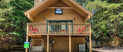 A two-story wooden cabin with a balcony, surrounded by trees.