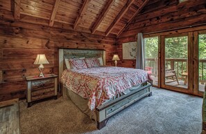 Un dormitorio de cabaña de madera con cama, mesitas de noche y vistas al exterior.