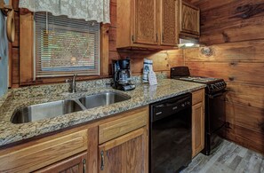 A kitchen with granite countertops, wooden cabinets, a stainless steel sink, a coffee maker, and a stove.
