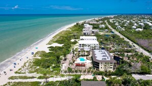 Eine Luftaufnahme eines Küstenresorts mit Strand, mehreren Gebäuden und einem Schwimmbad.