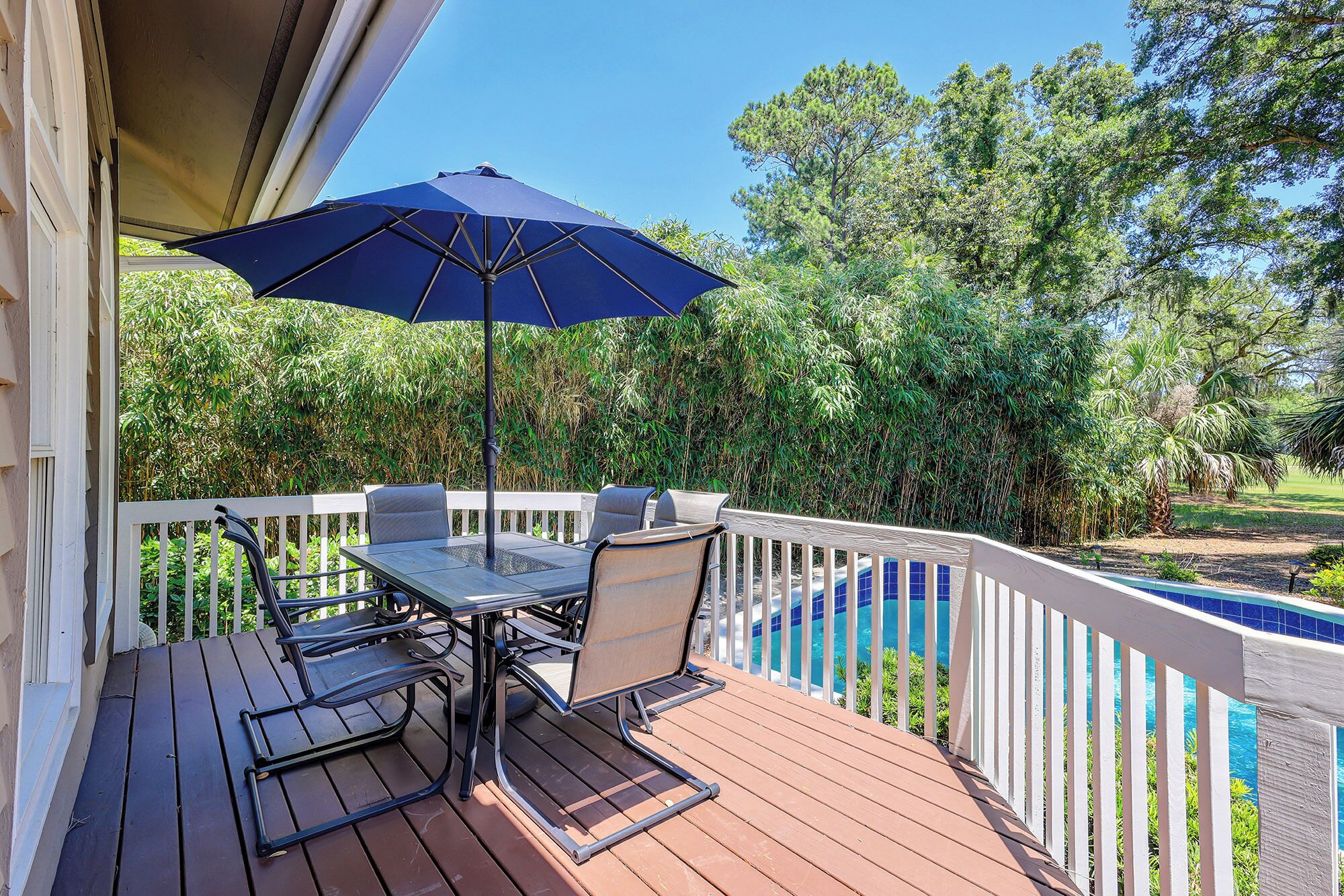Une terrasse en bois avec une table et des chaises, un parasol bleu et une piscine en arrière-plan.