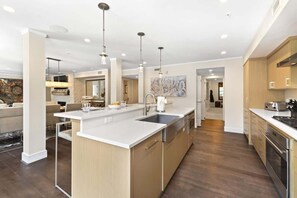 Une cuisine moderne dotée d’un îlot central, d’appareils électroménagers en acier inoxydable et de luminaires suspendus.