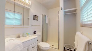 A modern bathroom with a white vanity, a toilet, a shower with a glass door, and a white laundry basket.