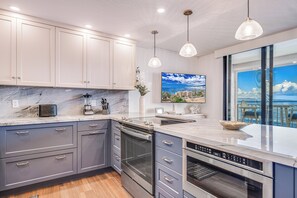 Une cuisine moderne avec des meubles gris, un plan de travail en marbre, des appareils électroménagers en acier inoxydable et des luminaires suspendus.