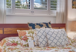 Un lit avec une literie à motifs floraux, une tête de lit en bois et une fenêtre avec des stores.