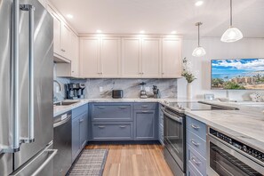 A modern kitchen with stainless steel appliances, light blue cabinets, and a marble countertop.
