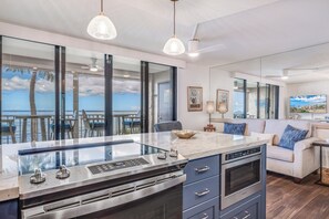 Une cuisine moderne dotée d’un grand îlot central, d’un four encastré et offrant une vue sur l’océan.