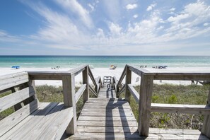 Une promenade en bois qui mène à une plage, avec un ciel dégagé et une mer calme.