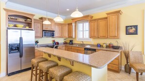 A kitchen with wooden cabinets, a stainless steel refrigerator, a granite countertop, and three woven bar stools.