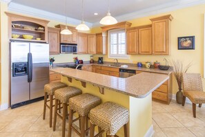 A kitchen with wooden cabinets, a stainless steel refrigerator, a granite countertop, and three woven bar stools. - End of Journey #201 - End Unit, Elevator, Gulf Front at Dune Allen Beach (Santa Rosa Beach)