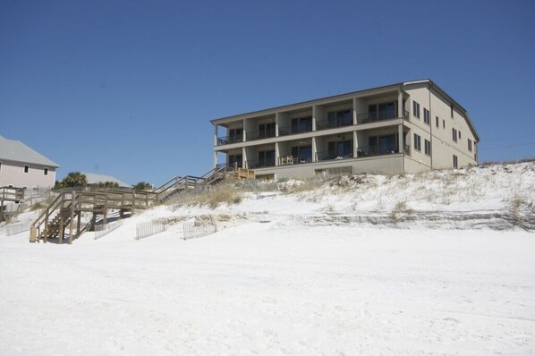 A multi-story building with a flat roof, located on a sandy beach with a staircase leading up to it.