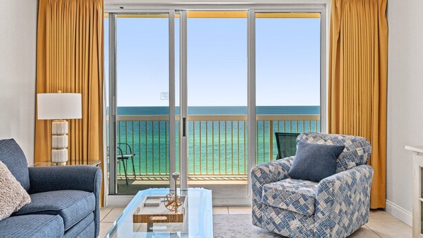 Quarto com sofá, poltrona e mesa de centro de vidro. Vista para o oceano através de grandes portas deslizantes.