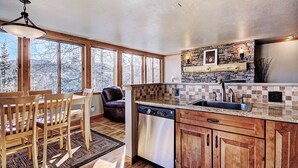 A kitchen with wooden cabinets, a stone backsplash, a built-in dishwasher, and large windows offering a view of snow-covered trees.