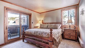 A bedroom with a wooden bed, a nightstand, a lamp, and a sliding glass door leading to a balcony.