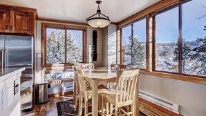 A kitchen with a dining area, large windows, and a view of snow-covered trees.