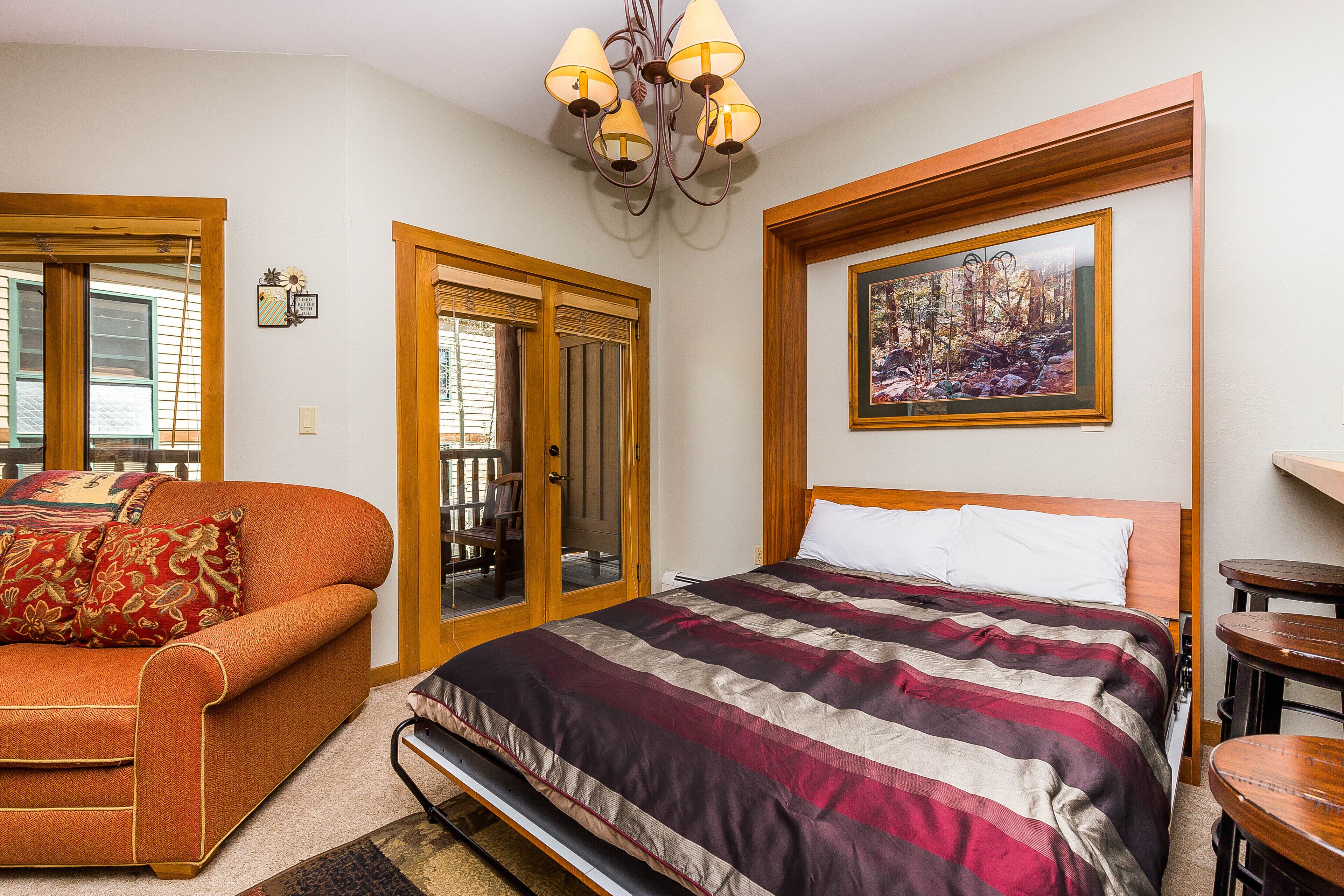 Un dormitorio con cama, sofá, candelabro, un cuadro y una puerta que da a un balcón.