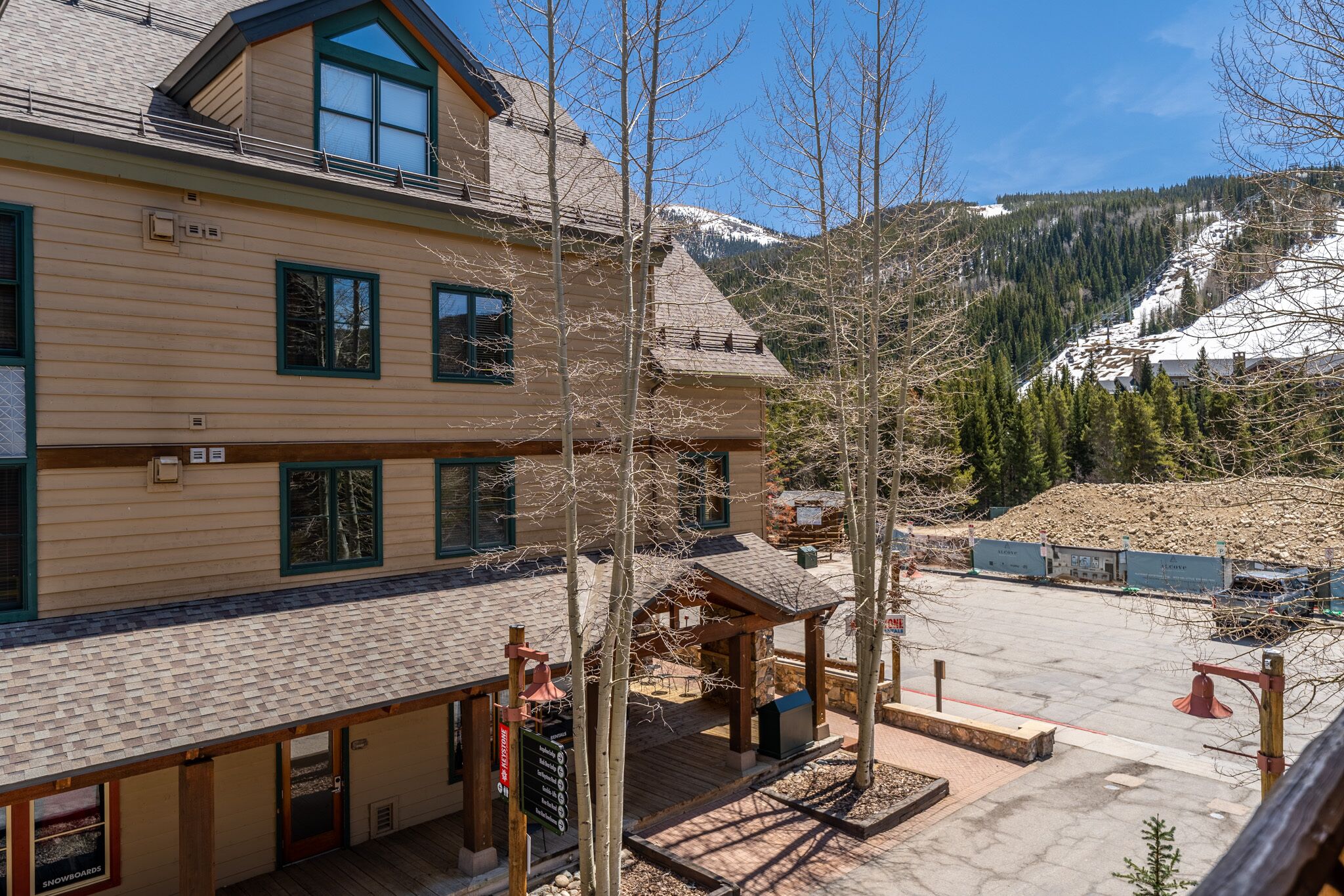 A lodge with a covered patio, a snow-covered mountain in the background, and a clear sky.