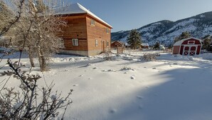 Una cabaña de madera con un paisaje nevado y montañas al fondo.