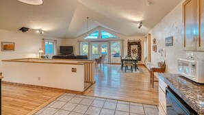 Amplia sala de estar con cocina, mesa de comedor y un gran ventanal con vistas a un paisaje pintoresco.