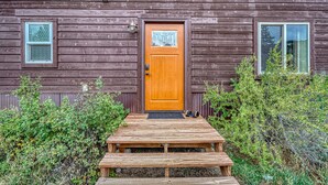 Una cabaña de madera con una puerta principal, dos ventanas y una terraza de madera que conduce a la puerta.