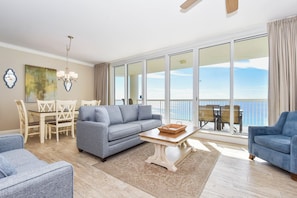 A spacious living room with a large sofa, a coffee table, and a dining area with a table and chairs. - Beachfront Condo w/ Gulf Views & Private Balcony in Destin! 💙🌴🌅 (Destin)