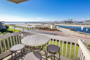 Un balcon avec une table et deux chaises donnant sur une plage et un port de plaisance.