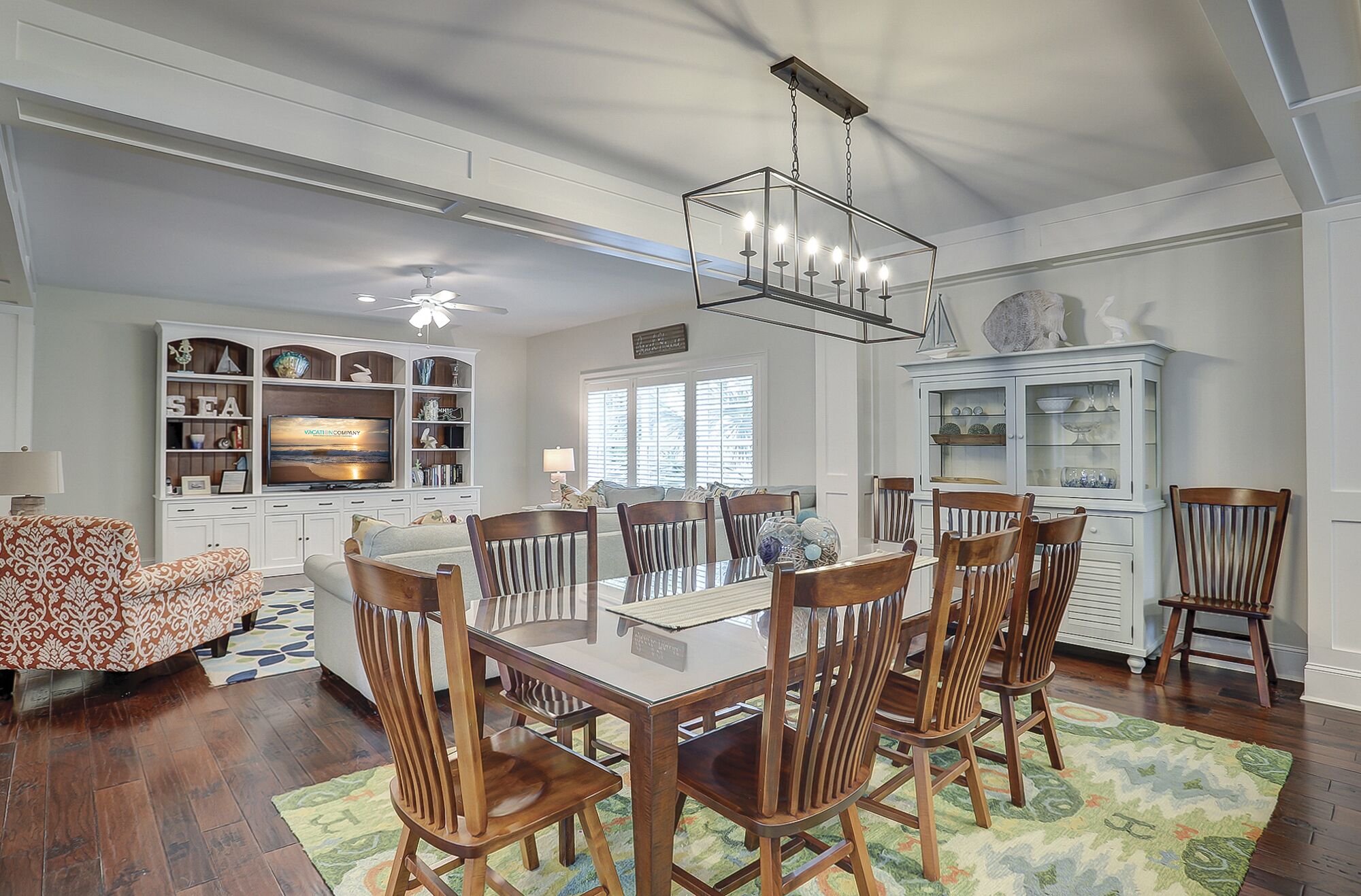 A spacious dining area with a glass-top table surrounded by wooden chairs, a chandelier, and a large white cabinet with glass doors.