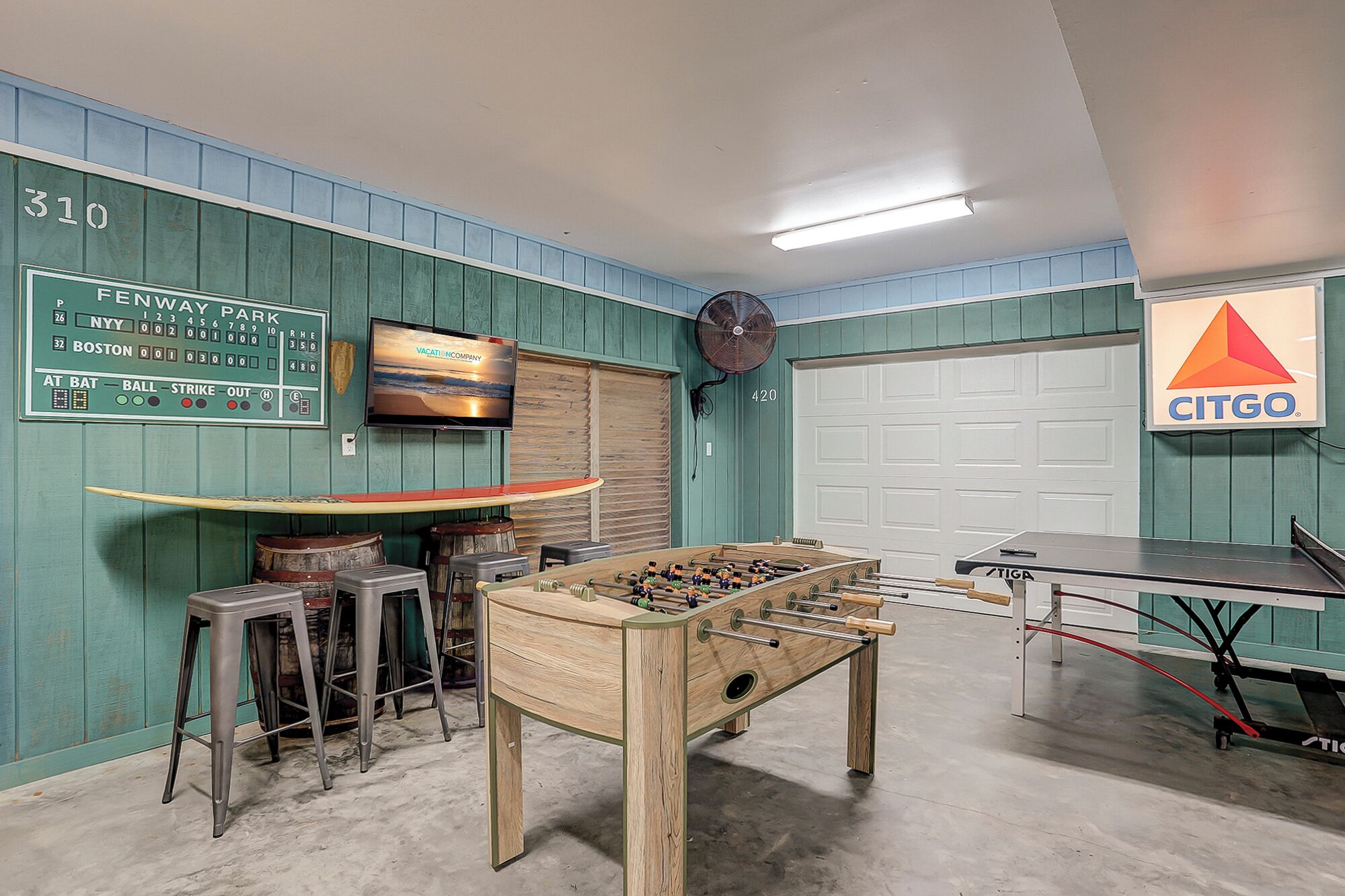 Een kamer met een tafelvoetbaltafel, een pingpongtafel en een televisie waarop een honkbalwedstrijd wordt vertoond.