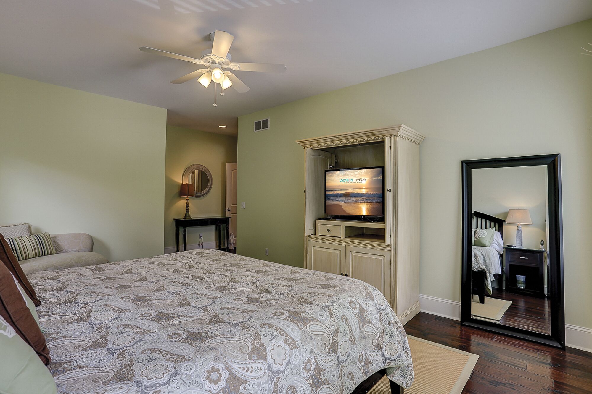 Une chambre à coucher avec un lit, un téléviseur posé sur un meuble, un ventilateur de plafond et un grand miroir.