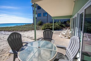 Une terrasse avec une table ronde et quatre chaises Adirondack, donnant sur une plage et l’océan.