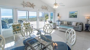 A spacious living room with a glass door leading to a balcony, a gray sofa, and a dining area with chairs and a table. - GULF FRONT! Pet Friendly! Beach Cottage 30A- Dune Allen Beach (Santa Rosa Beach)