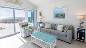 A living room with a view of the beach, a sofa, a patterned armchair, and a coffee table. - GULF FRONT! Pet Friendly! Beach Cottage 30A- Dune Allen Beach (Santa Rosa Beach)