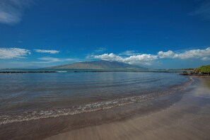 A beach with a rocky shoreline, calm water, and a mountain in the distance.