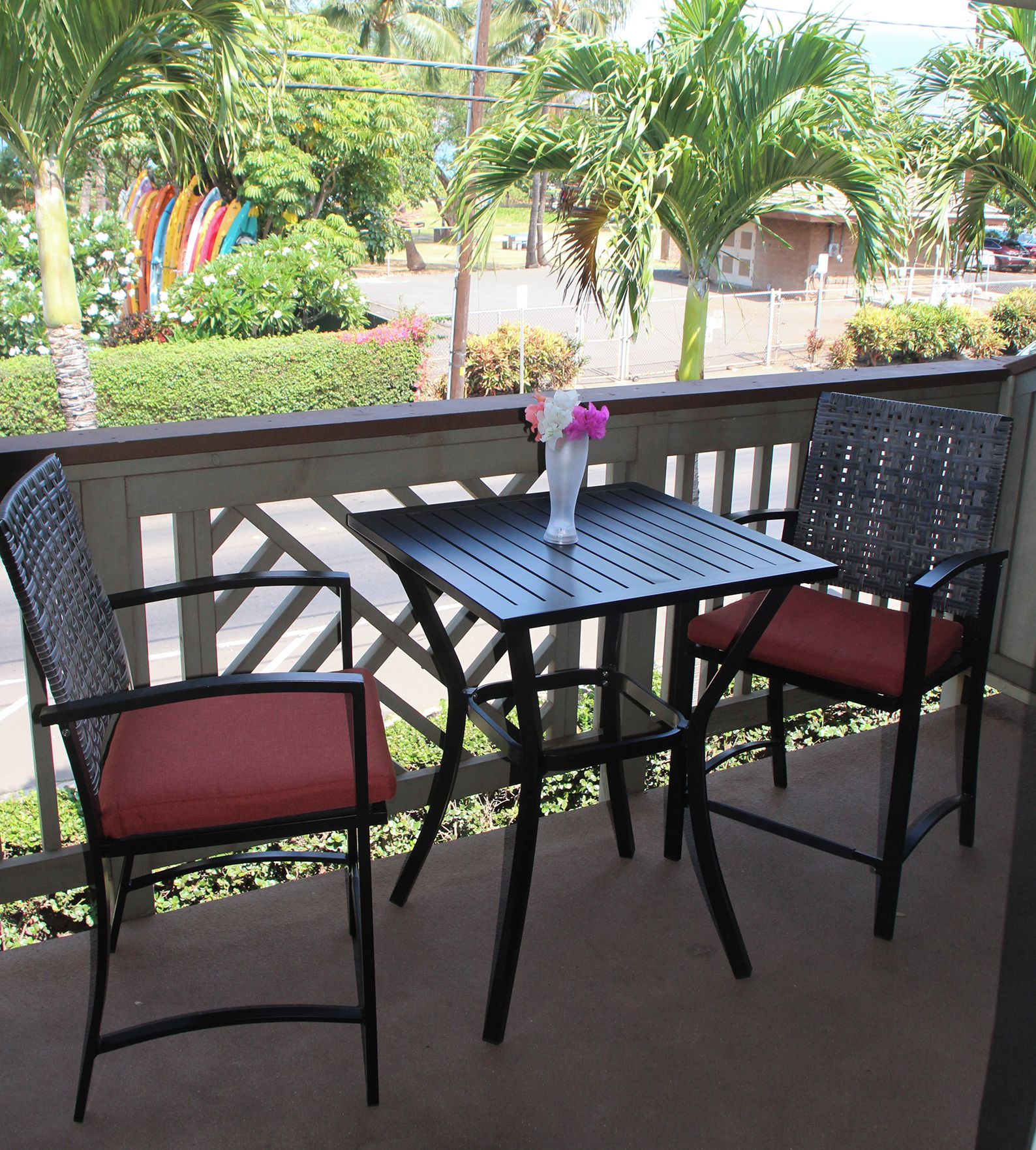 A patio with two chairs and a table, surrounded by a wooden fence and palm trees.