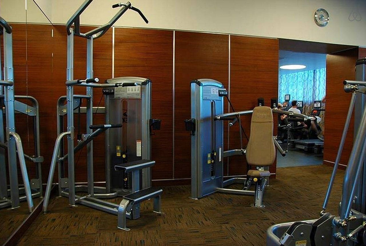 A gym with various exercise machines, including a squat rack and a bench press.