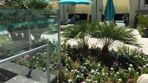 Ein Hotelinnenhof mit Außenbestuhlung, Palmen und Blumenbeeten.