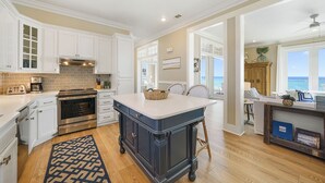 Una cocina con armarios blancos, una isla central y vistas al salón.